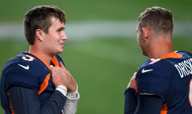 Drew Lock #3 of the Denver Broncos talks to Jeff Driskel #9 in the bench area during a game against...