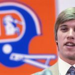 (Original Caption) John Elway, picked by Broncos in NFL draft, standing alone at a press conference with the Denver Broncos Logo in the background.
