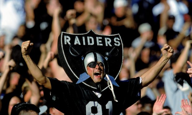 A fan of the Oakland Raiders cheers in the stands as he wears the logo during a game against the Ne...