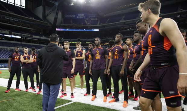 A group of wide receivers and quarterbacks listen as they prepare to have measurements taken during...