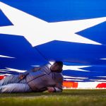 DENVER, CO - DECEMBER 29:  Kenneth Thompson lies under the American Flag as the National Anthem plays before a game between the Denver Broncos and the Oakland Raiders at Empower Field at Mile High on December 29, 2019 in Denver, Colorado. (Photo by Justin Edmonds/Getty Images)