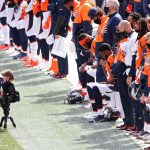 A videographer films members of the Denver Broncos as they stand and kneel during the U.S. National Anthem before playing against the Tampa Bay Buccaneers at Empower Field At Mile High on September 27, 2020 in Denver, Colorado. (Photo by Matthew Stockman/Getty Images)