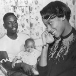 Braves' pennant drive hero looking forward to series Milwaukee, Wisconsin...Hank Aaron, Milwaukee Braves slugger whose home run broke up the game which clinched the National League pennant, is shown relaxing in his home while Mrs. Aaron receives his fans congratulatory calls. Hank is holding his six-months-old son Henry Jr. This is the first pennant for the Braves since there move from Boston to Milwaukee. Hank is looking forward to the Braves' world series battle against the New York Yankees.