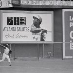 Hank Aaron's target for next year hangs over his head as he mans his left field position in the 9th inning, after he failed to get his one home run to tie Babe Ruth. As the home run chart says, Aaron will stand at 713 home runs until next season.
