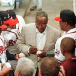 Hank Aaron (C) signs autographs for some of the Atlanta Braves players before ceremonies that unveiled the Hank Aaron Award on the 25th anniversary of his historic 755th home run 08 April 1999. The Hank Aaron Award will be based on the player's combined numbers of hits, home runs and RBI and is scheduled to be presented to the best hitter in each league Championship Series.        AFP PHOTO/STEVE SCHAEFER (Photo credit should read STEVE SCHAEFER/AFP via Getty Images)