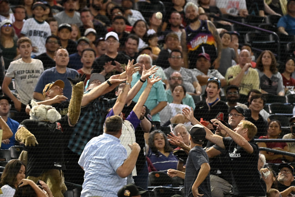 PHOENIX, ARIZONA - JUNE 03: Baxter the Arizona Diamondbacks mascot and other fans attempt to catch ...