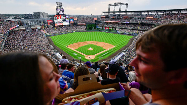 DENVER, COLORADO - JULY 3: Reported attendance of 47,665 fills the stadium as a pair of fans prepare to enjoy a large hot dog during a game between the Colorado Rockies and the San Francisco Giants at Coors Field on July 3, 2026 in Denver,